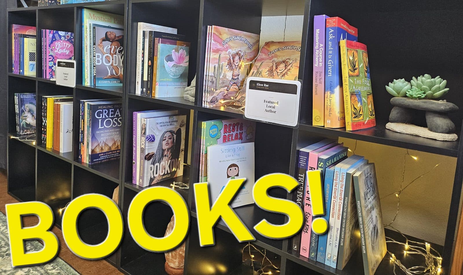 Black cube shelves filled with books and strung with fairy lights, captioned “Books!”.