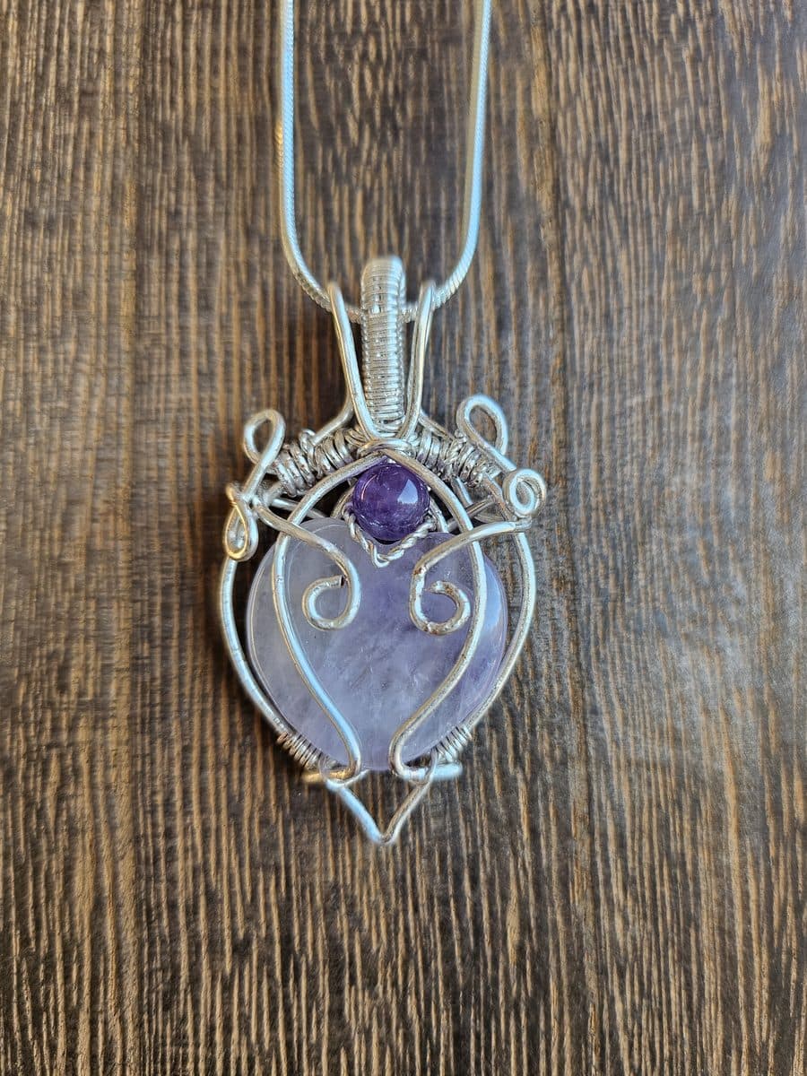 A pale amethyst heart pendant framed in silver wire scrollwork, hanging from a snake chain.