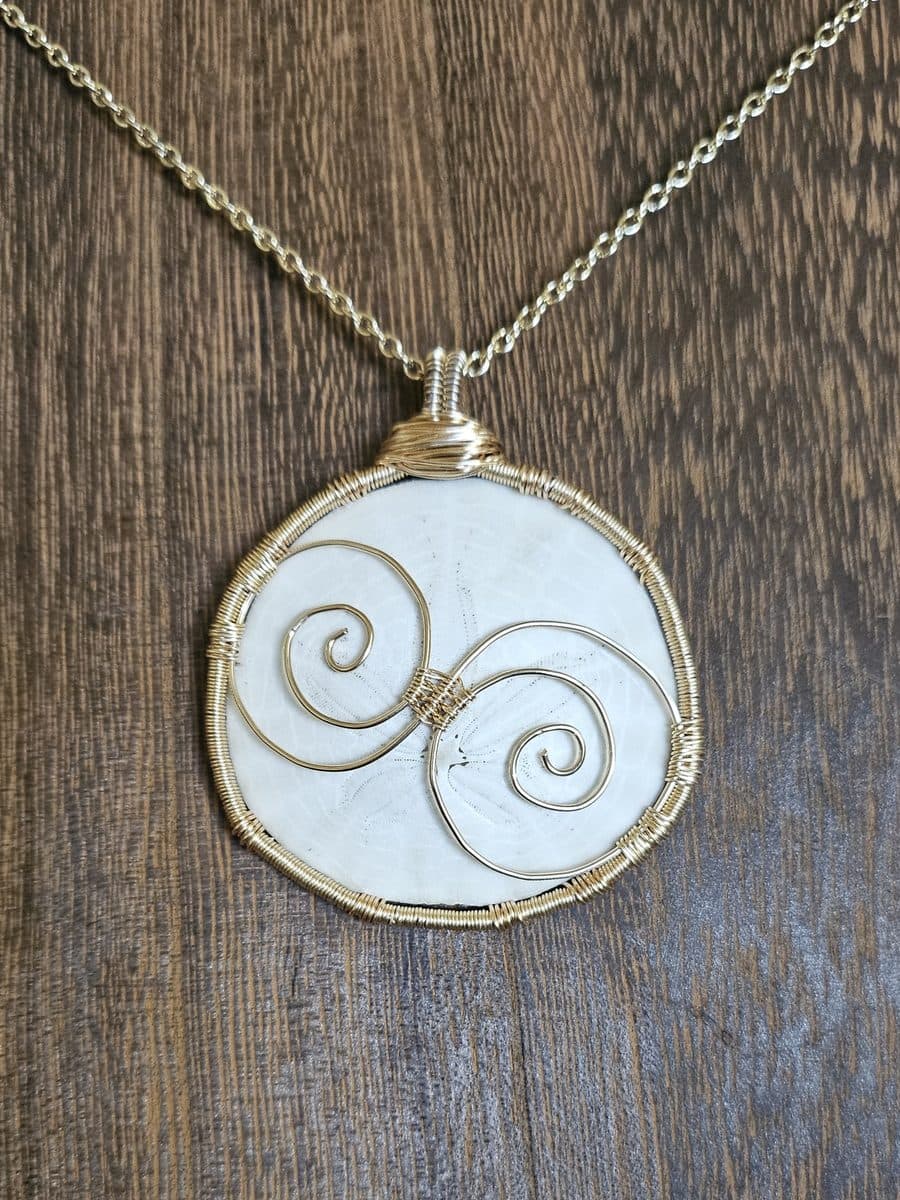 A round white stone wrapped in gold wire with two facing spirals, on a gold chain.