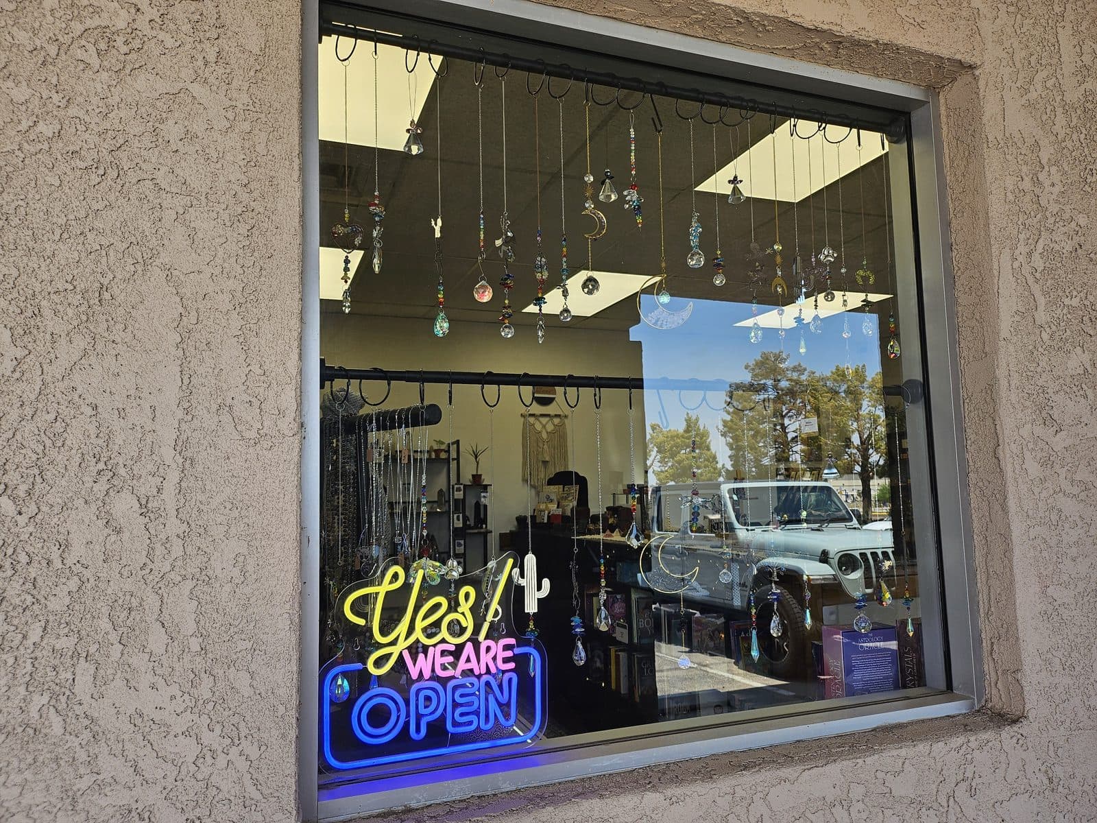 The Sixth House storefront window hung with crystal suncatchers behind a neon “Yes! We are open” sign.